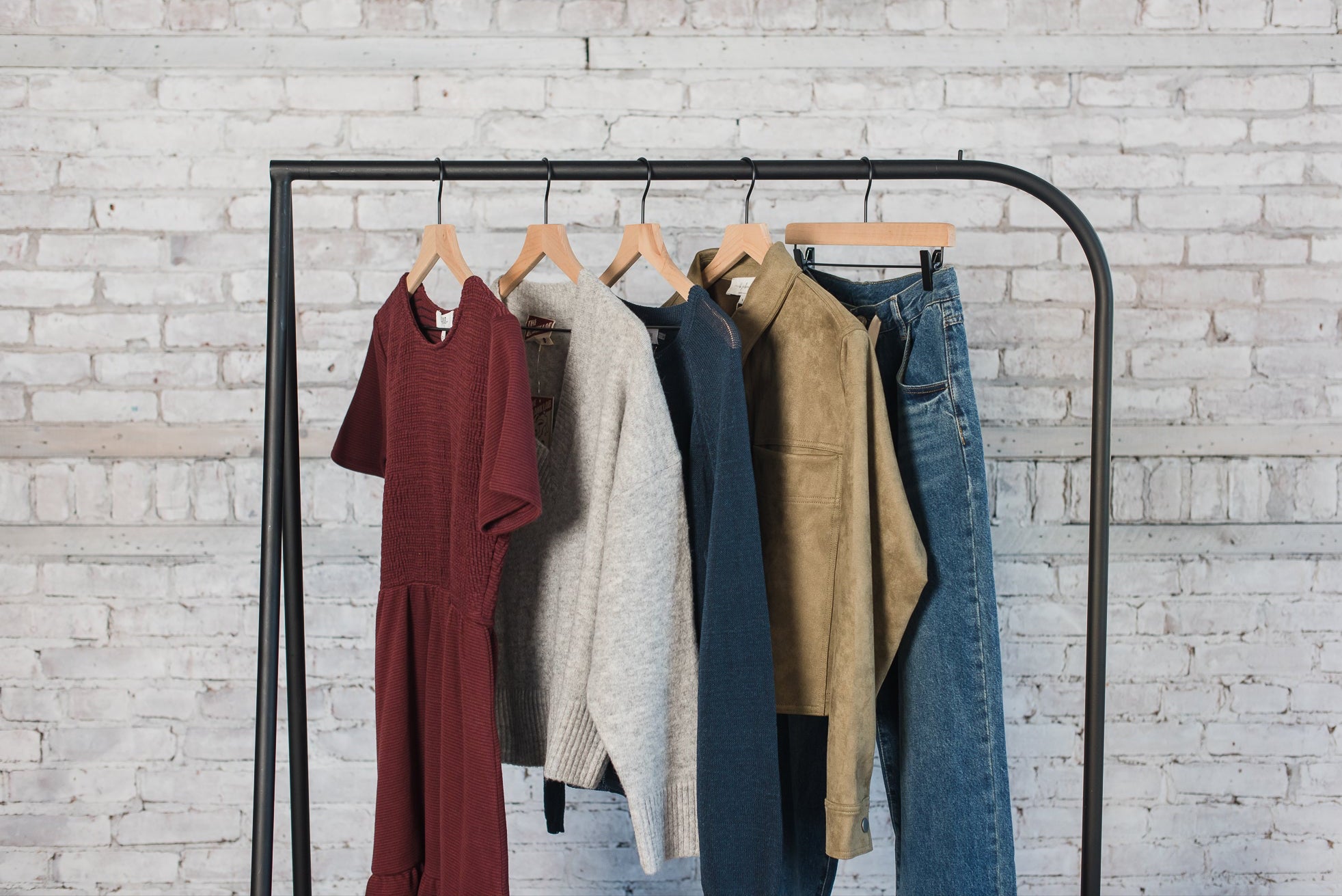 Clothing rack with various garments against a light brick wall.